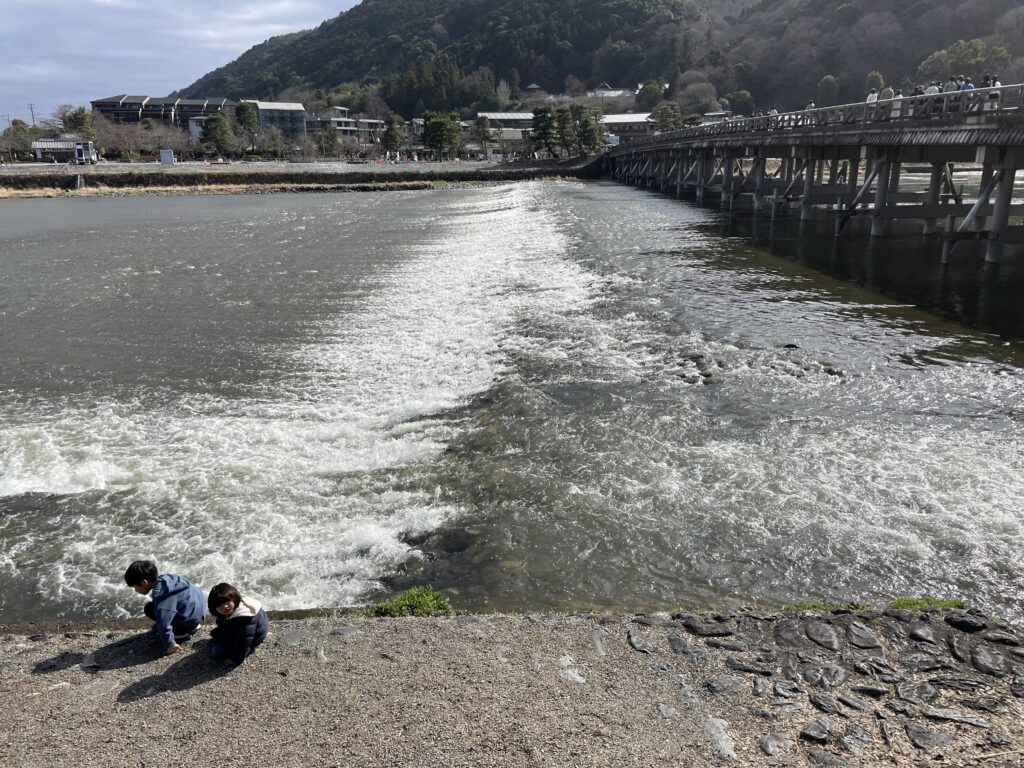 桂川の河原で遊ぶ子どもたちと渡月橋