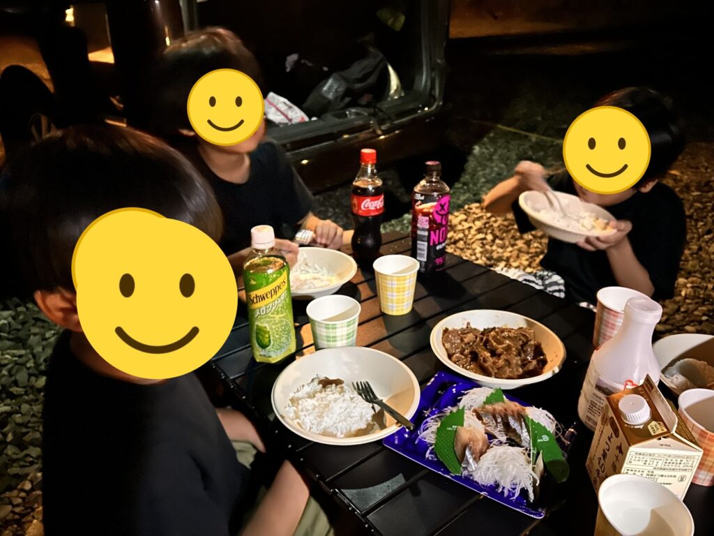 夜の車の横で夕食をとる子どもたち