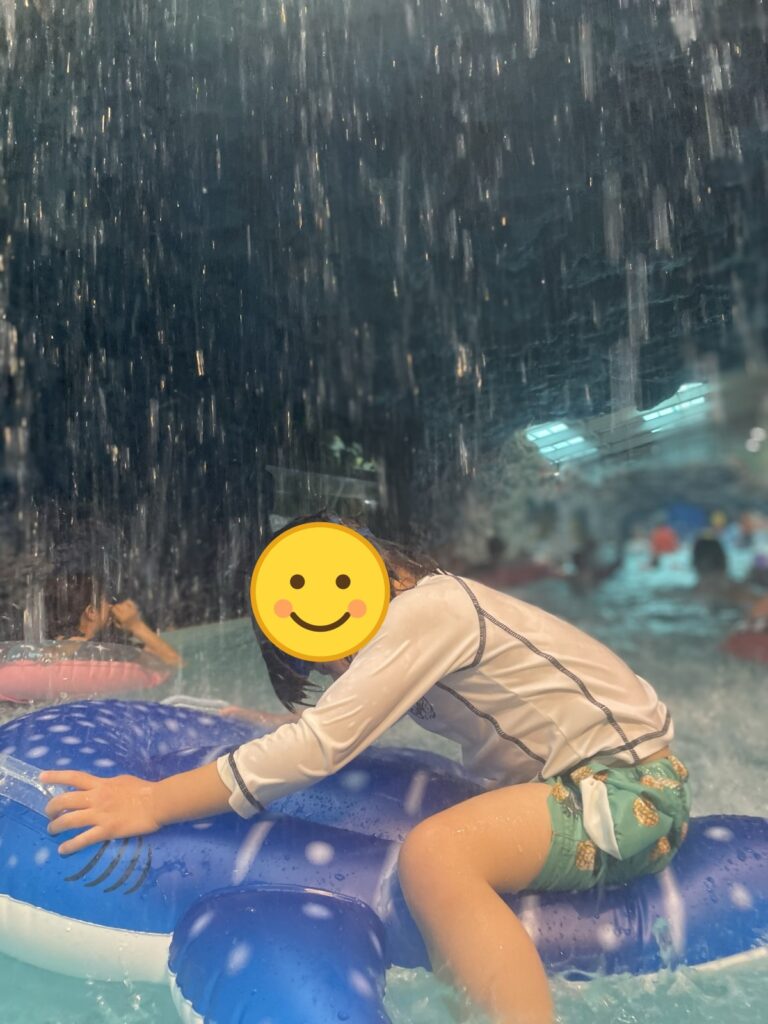 滝の下で浮き輪にしがみつく子ども