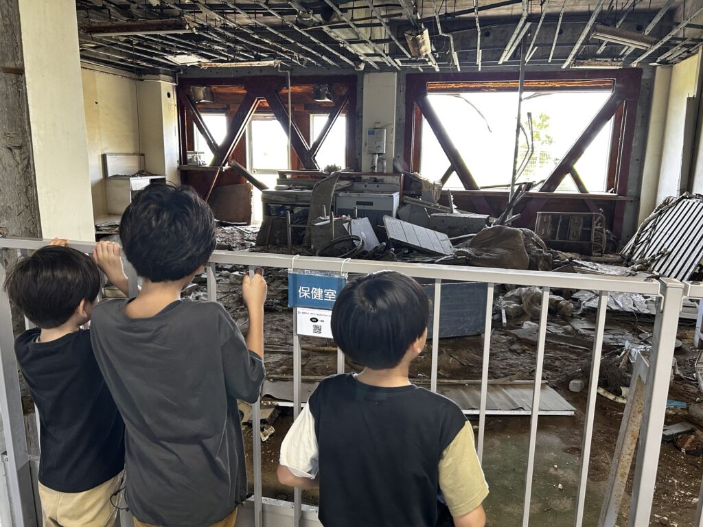 震災遺構の校舎で、津波で流れ込んだ残骸を見る子どもたち