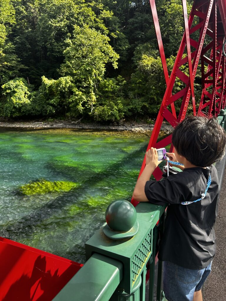 支笏湖の近くの赤い鉄橋と透き通った緑色の水面でカメラを構える子ども