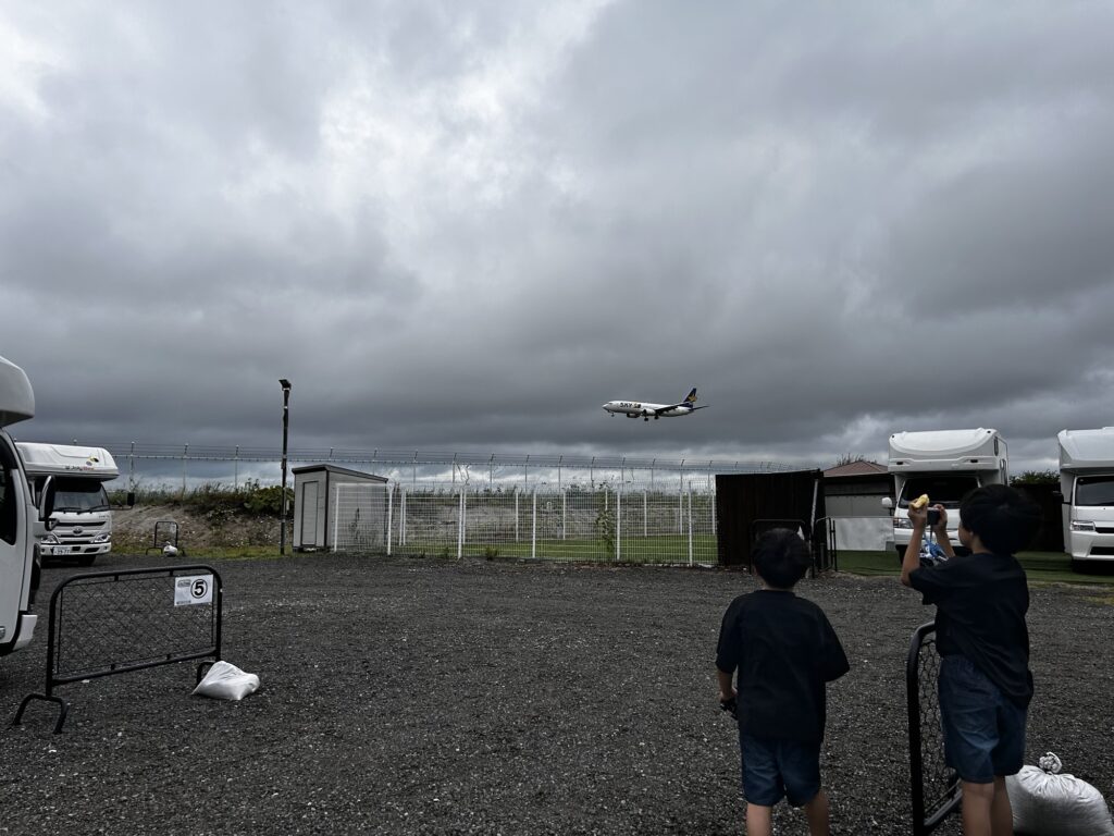 曇り空の下、滑走路に着陸する飛行機を眺める親子