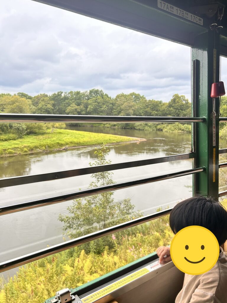 ノロッコ号の窓から湿原の川を眺める子ども(顔はスタンプで加工)