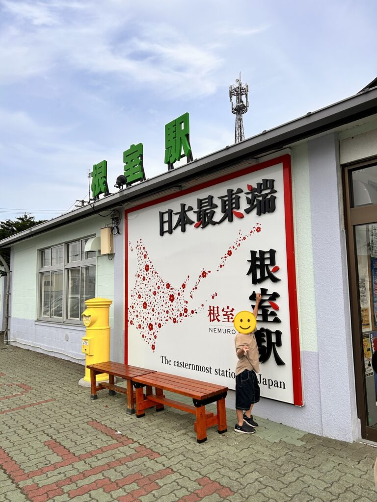 日本最東端の根室駅の看板の前でポーズをとる子ども(顔はスタンプで加工)