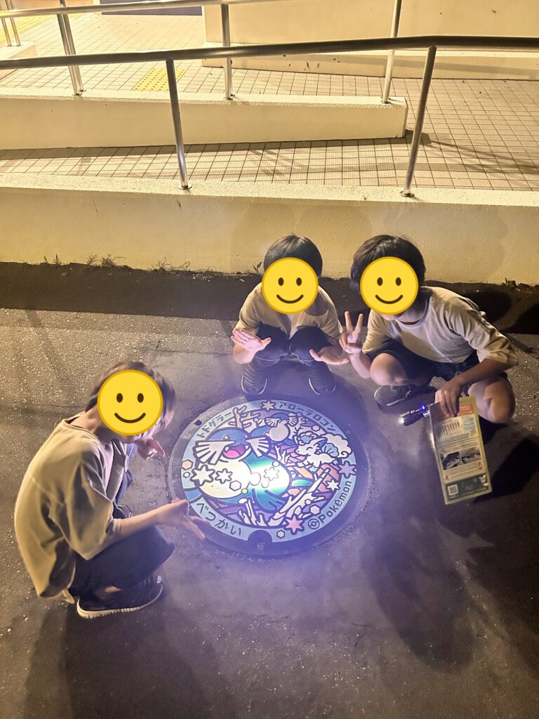 夜にポケモンのご当地マンホール「ポケふた」の前でポーズをとる三兄弟(顔はスタンプで加工)