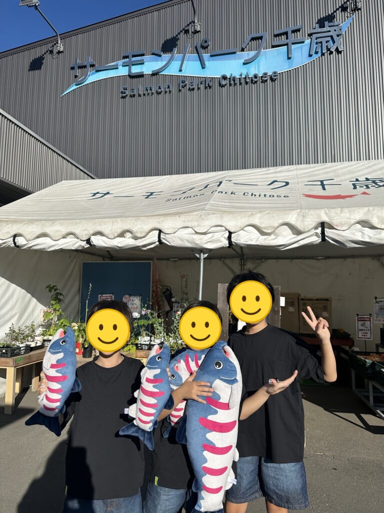 サーモンパーク千歳でサケのぬいぐるみを抱える三兄弟(顔はスタンプで加工)