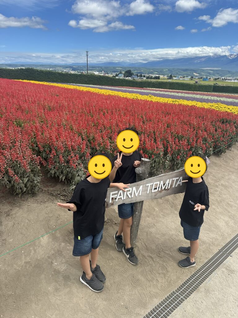 冨田ファームの看板の前でポーズをとる三兄弟(顔はスタンプで加工)